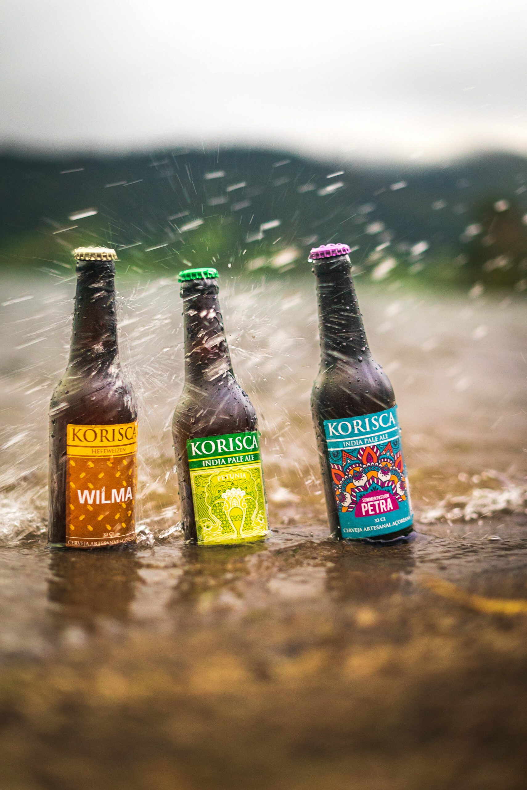 Three Korisca craft beers, the Wilma (Hefeweizen), the Petunia (IPA) and the Petra (IPA), inside the Sete Cidades Lagoon, with splashes and the green valley in the backgroundSete Cidades, Ponta Delgada, São Miguel, Azores.