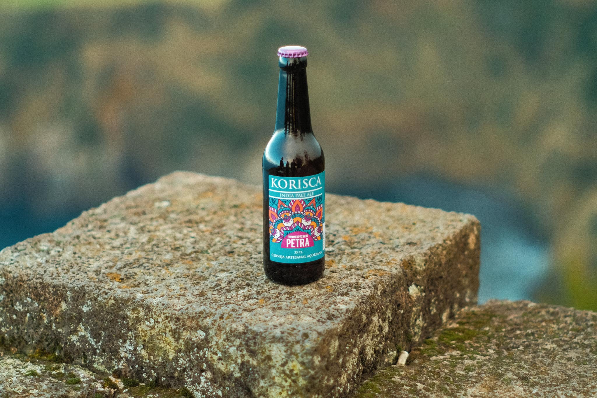 Cerveja artesanal açoriana Korisca Petra (IPA), em cima do muro de pedra branca, com o mar azul e a costa da ilha de São Miguel, no Miradouro de Santa Iria, Ribeira Grande, São Miguel, Açores.